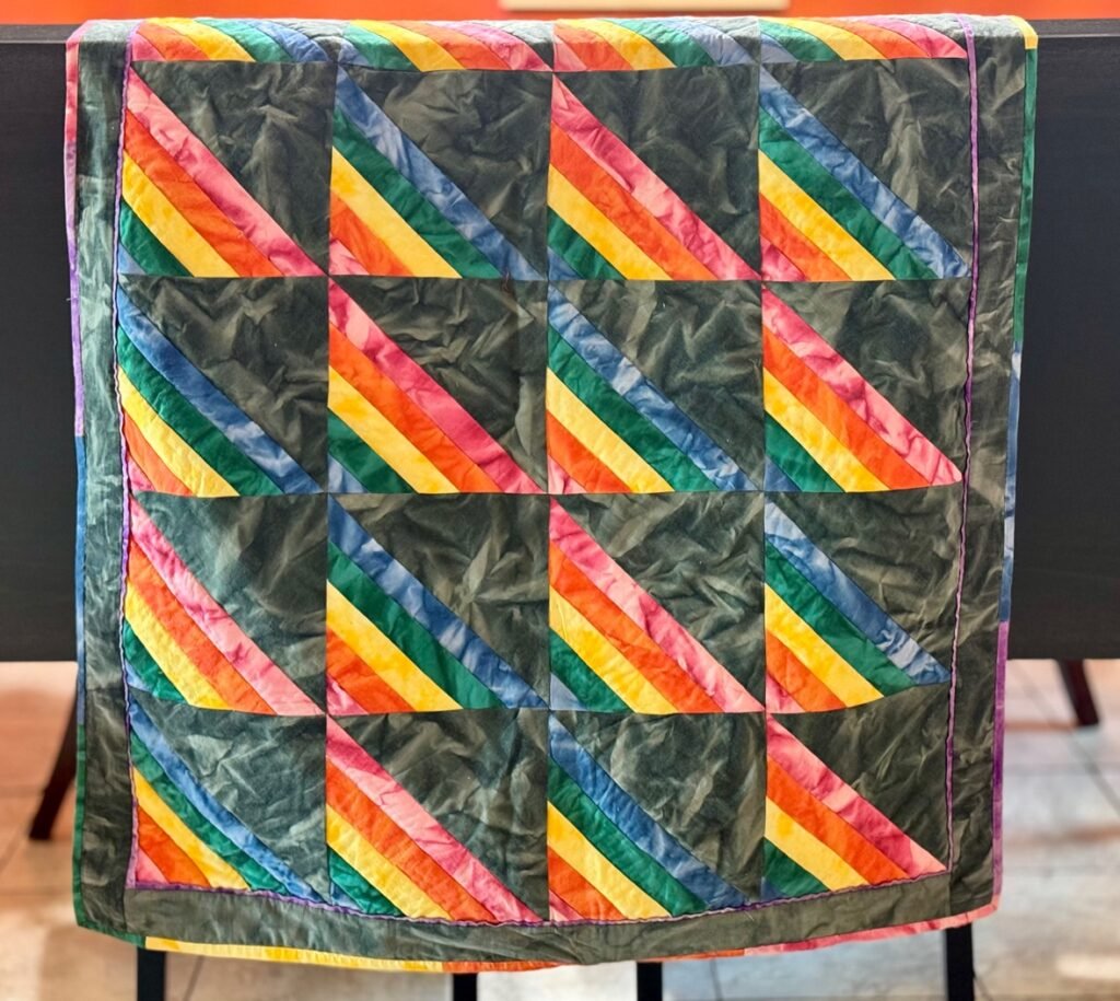 Rainbow palette quilt set in black, hanging on a banister