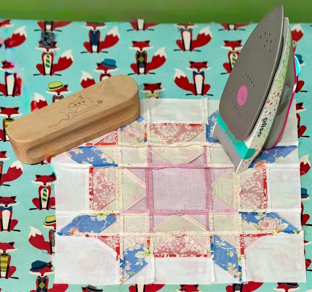 Starfish block being pressed, showing the seams, with an iron and wooden clapper